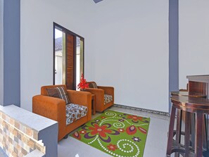 Ein Wohnzimmer mit zwei orangefarbenen Sofas, einem gemusterten grünen Teppich und einem Holztisch.