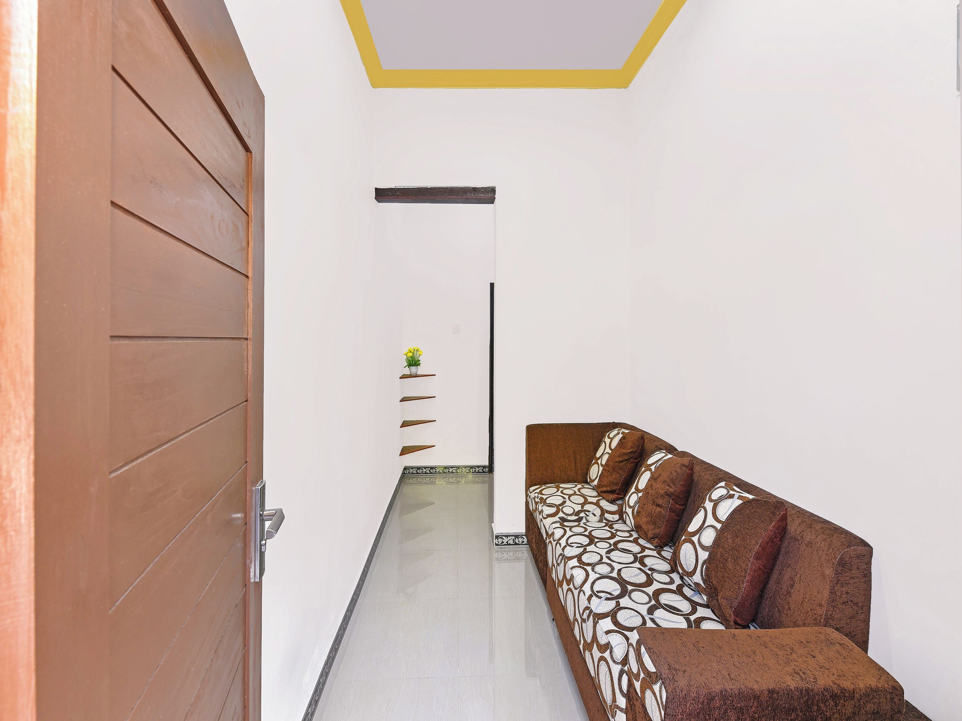 Un corridoio con una porta in legno, un divano con cuscini decorati e una piccola pianta su uno scaffale.