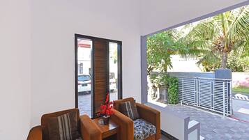 Una sala de estar moderna con dos sofás y una mesa de centro, ventanas amplias que dan a la calle y zonas verdes.