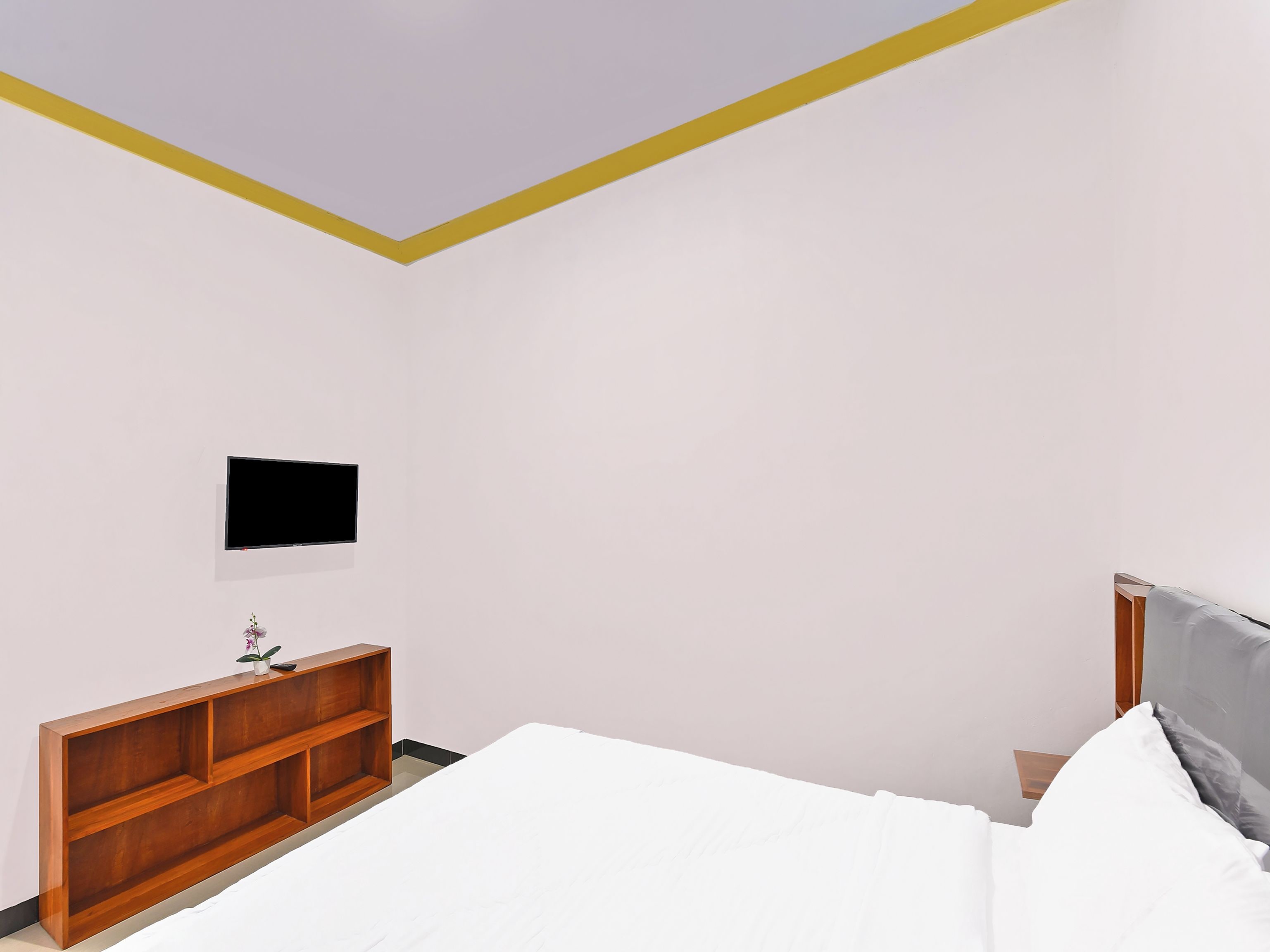A bedroom with a bed, a wooden nightstand, a television mounted on the wall, and a small shelf with a plant.