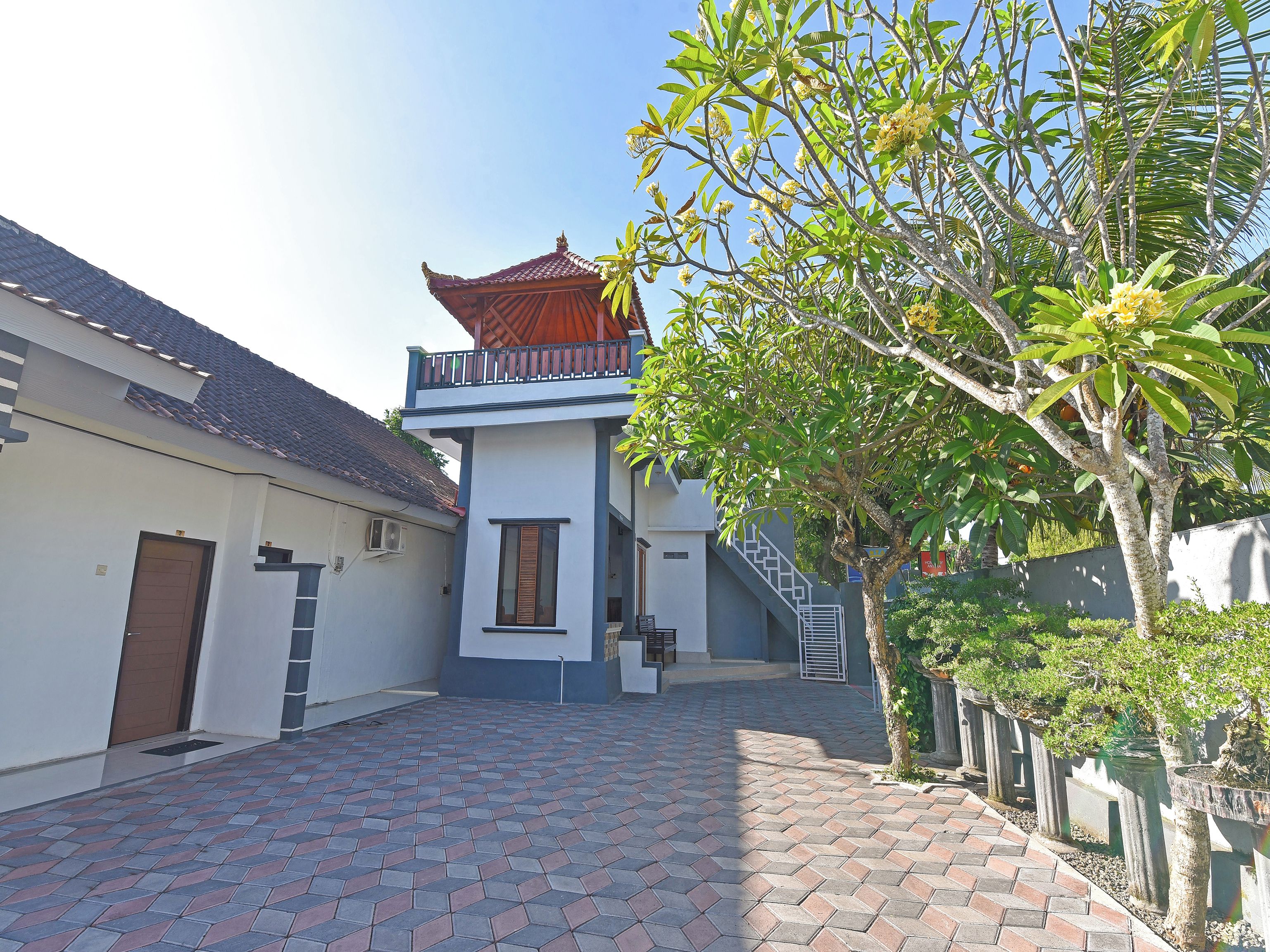 A courtyard with a tiled floor, a building with a traditional roof, and a tree with green leaves.