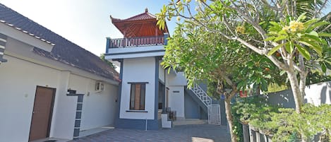 A courtyard with a tiled floor, a building with a traditional roof, and a tree with green leaves.
