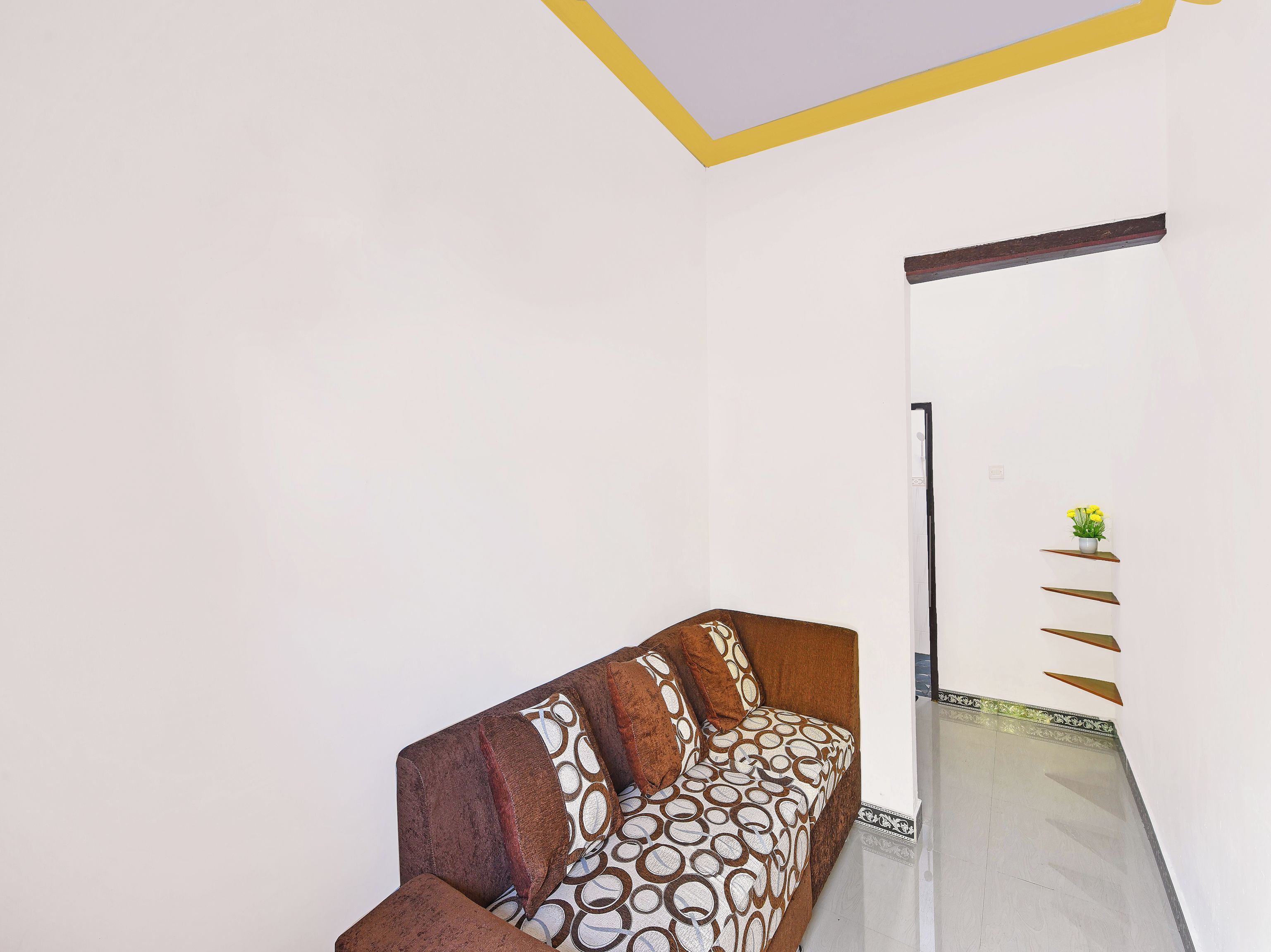 Una habitación con sofá, una estantería empotrada con una planta y un techo decorativo.