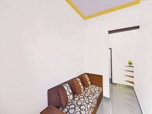 A room with a sofa, a wall-mounted shelf with a plant, and a decorative ceiling. - OYO 91192 Homestay Antara (Melaya)