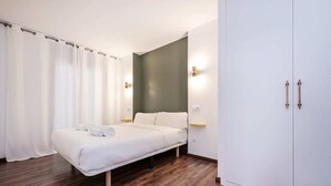 Un dormitorio con cama, cortinas blancas, un armario y una mesita de noche con lámpara.