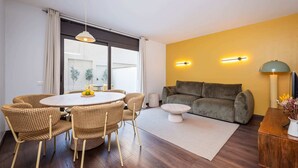 Una sala de estar moderna con una mesa de comedor redonda, sillas de mimbre, un sofá gris y una pequeña mesa de centro blanca.