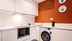 Een kleine keuken met een magnetron, oven en wasmachine.
