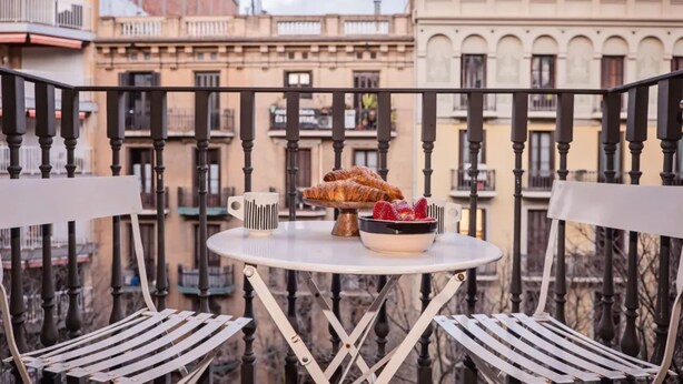 A balcony with a table set for breakfast, including croissants and strawberries, overlooking a cityscape with traditional architecture. - Sweett | Bailen 204 - Two Bedroom Apartment, Sleeps 4 (Barcelona)