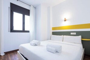 Ein Hotelzimmer mit Bett, zwei zusammengerollten Handtüchern, einem Fenster mit Vorhängen und einem Wandlichtschalter.