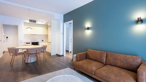 Ein modernes Wohnzimmer mit einem braunen Sofa, einem Esstisch mit Stühlen und einer Küchenzeile mit weißen Schränken und einer Mikrowelle.
