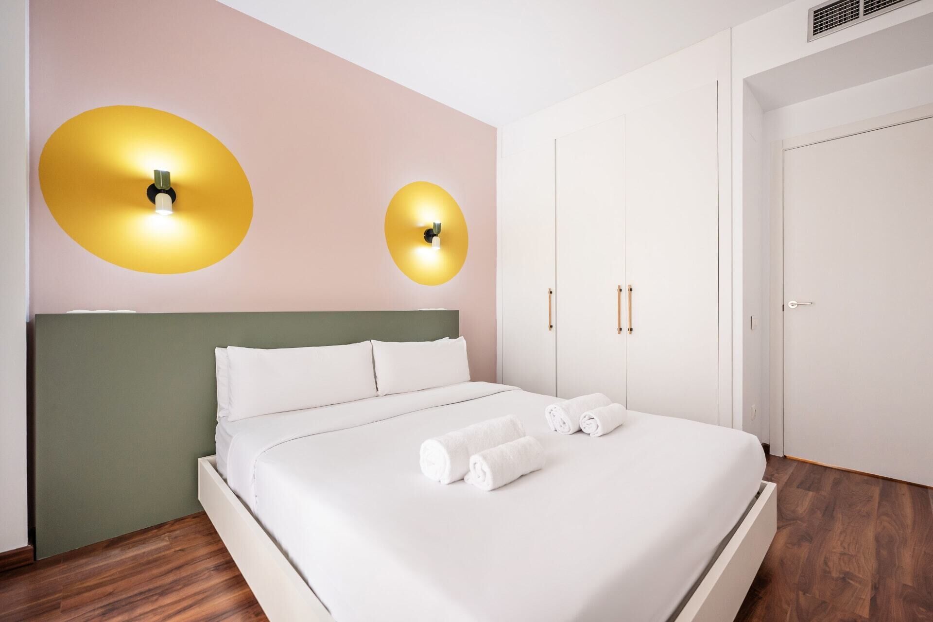 Una habitación de hotel moderna con una cama, dos lámparas de pared, un armario y suelo de madera.