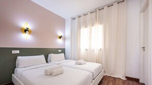 A hotel room with two beds, a wooden floor, a green accent wall, and a white door. - Sweett | Bailen 401 - Two Bedroom Apartment, Sleeps 4 (Barcelona)