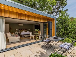 A modern, compact hotel room with a wooden ceiling, a bed, a sitting area with a table and chairs, and a view of the outdoors. - Charming Bosham Garden Lodge - Pass the Keys (Chichester)
