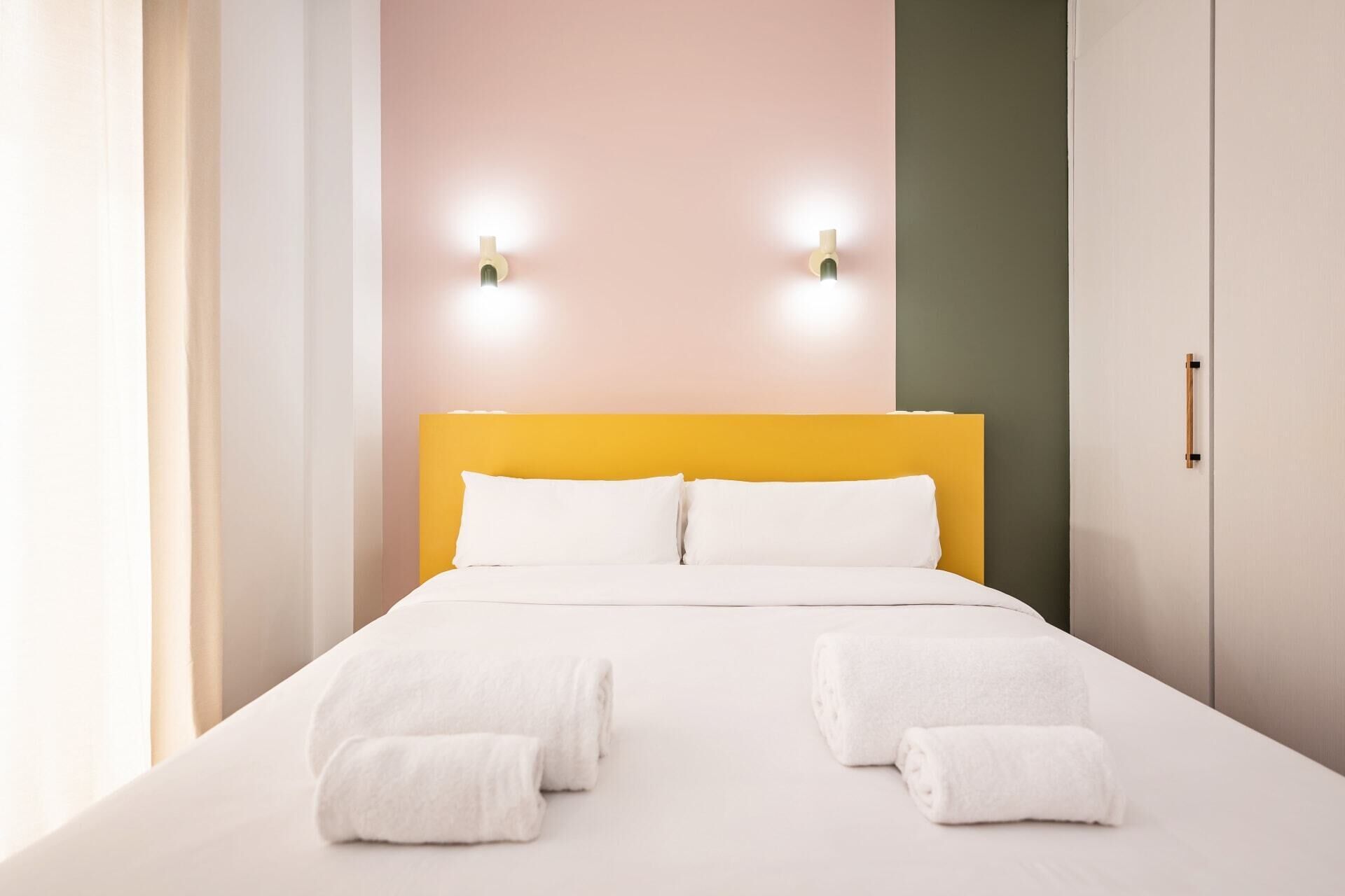Une chambre d’hôtel avec un lit, deux lampes fixées au mur et une porte dotée d’une poignée.