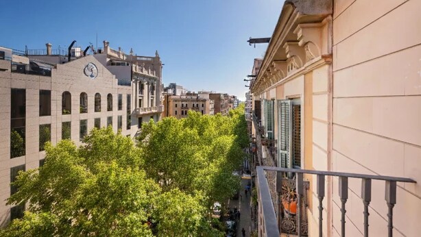 Una estrecha calle urbana con arquitectura tradicional, incluyendo un edificio con una torre de reloj y otro con un balcón.