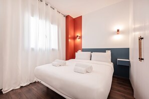 Habitación de hotel moderna con una cama grande, ropa de cama blanca, piso de madera y una pared de acento roja.