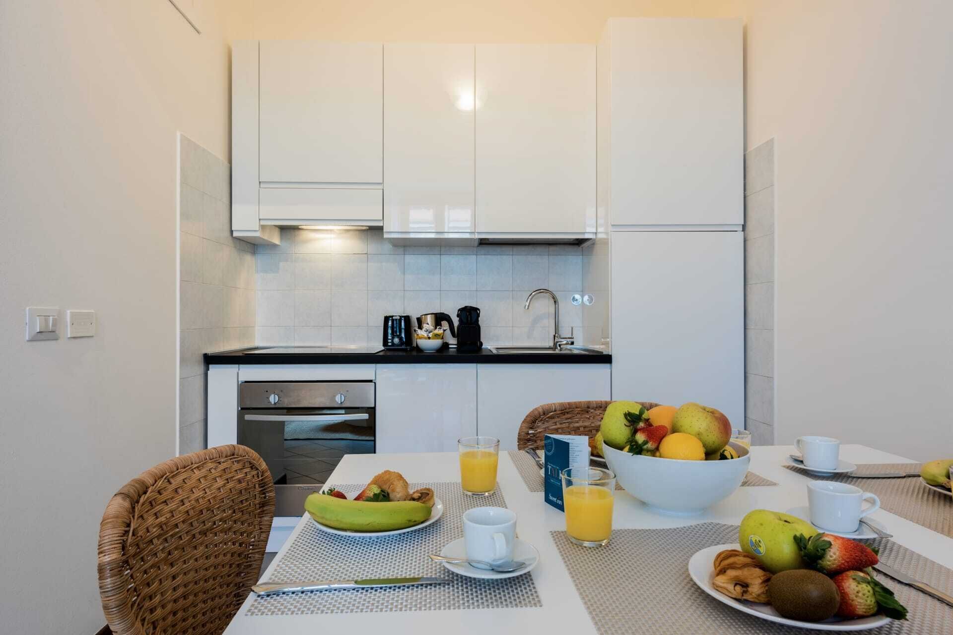 Et moderne køkken med hvide skabe, en sort bordplade og et spiseområde med et bord dækket til morgenmad.