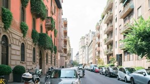 Una stretta via cittadina fiancheggiata da edifici a più piani, alcuni con balconi e vegetazione.