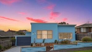 A modern two-story house with a blue exterior, large windows, and a small front yard with a bench and plants. - A-Wave from it All - 1960's Chic (Warrnambool)