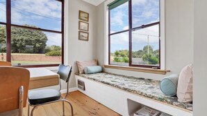 A room with a built-in bench along a large window, a desk, and a chair. - A-Wave from it All - 1960's Chic (Warrnambool)