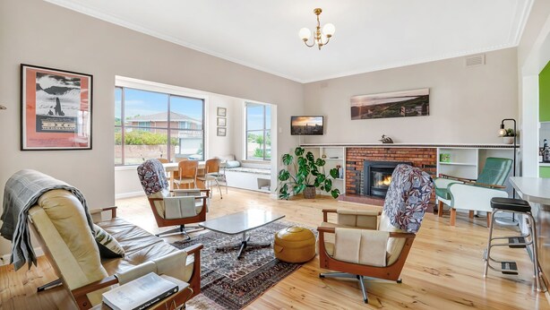 A spacious living room with a fireplace, large windows, and a dining area. - A-Wave from it All - 1960's Chic (Warrnambool)