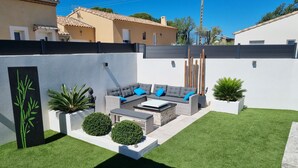 Un área de estar moderna al aire libre con un sofá gris, cojines azules y una mesita.
