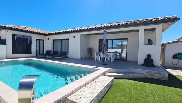 Una casa moderna con piscina, mobiliario exterior y una estatua.
