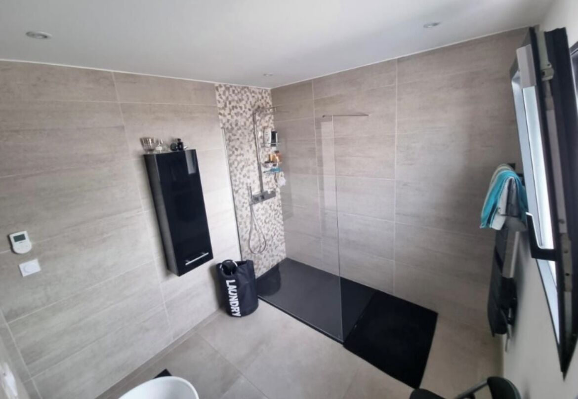 A modern bathroom with a shower, a toilet, and a sink. There is a towel rack and a black mat on the floor.