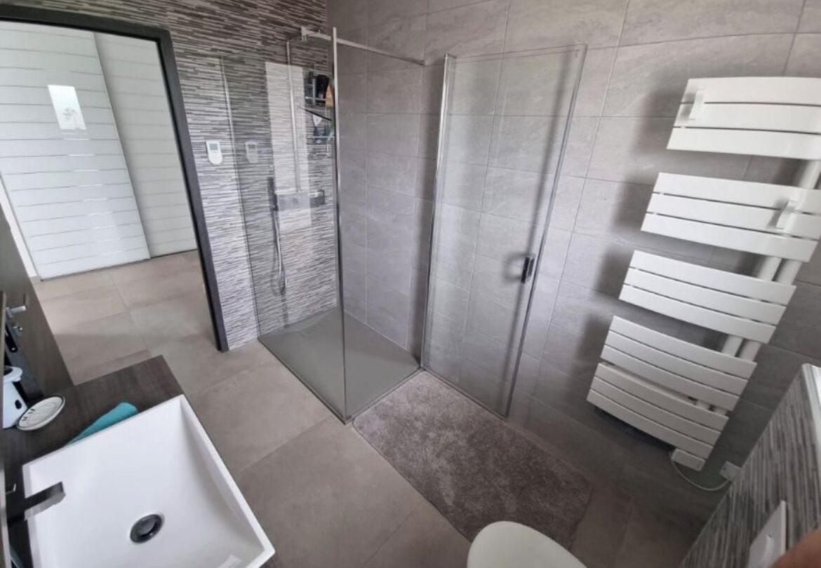 Ein modernes Badezimmer mit einer Duschkabine, einem weißen Waschbecken und einer Toilette.