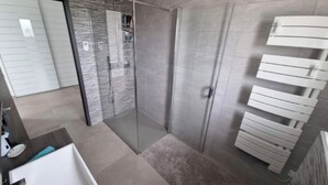 Un baño moderno con ducha de vidrio, lavamanos blanco y un inodoro.