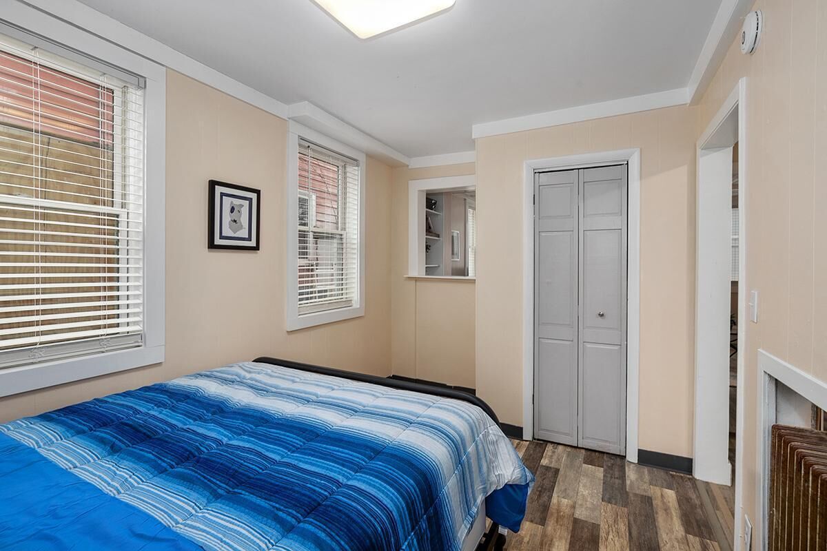 A bedroom with a bed, two windows with blinds, a door, and a small closet.