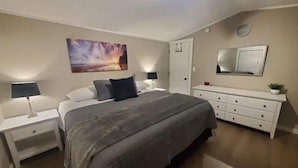 Une chambre à coucher avec un lit, des tables de chevet, une commode, un miroir et un tableau accroché au mur.