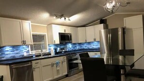 Une cuisine moderne avec des meubles blancs, des appareils en acier inoxydable, un plan de travail noir et une table à manger en verre.