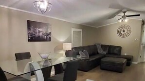 Un salon moderne avec une table à manger en verre, un canapé en cuir noir et un ventilateur de plafond.