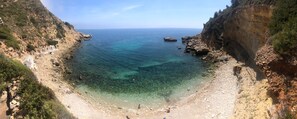 A coastal landscape with a rocky beach, clear water, and a cliff.