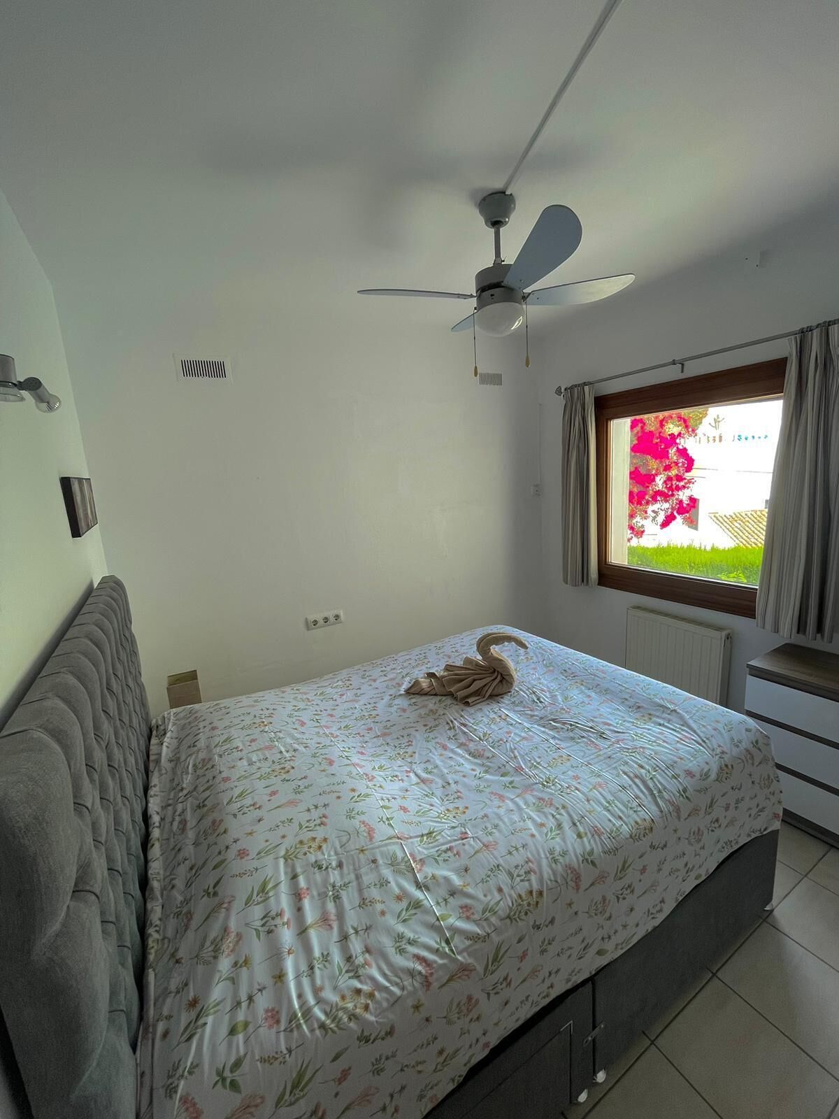 Un dormitorio con cama, ventilador de techo, ventana con cortinas y radiador.