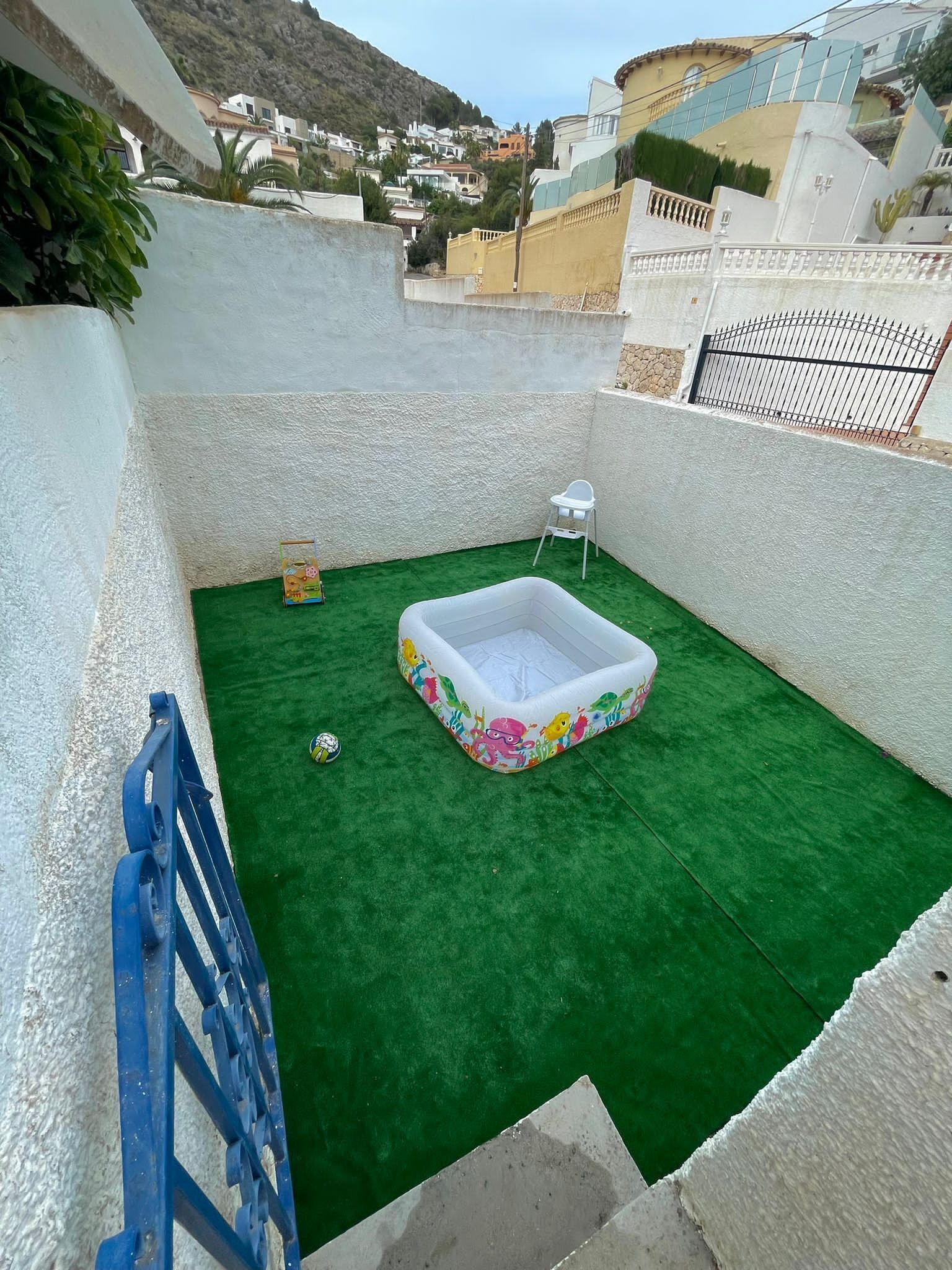 Eine Dachterrasse mit künstlichem Rasen, einem weißen aufblasbaren Pool und einem blauen Tor.