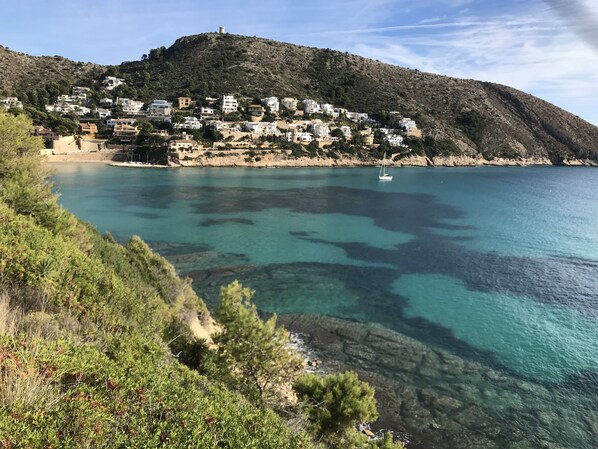 A coastal village with buildings on a hillside overlooking a clear blue sea.