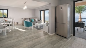 A modern living room with a grey sofa, a teal armchair, and a white coffee table. A large window offers a view of the sea. - Quality tranquil villa with sea-view | OceanScape (Poiso)