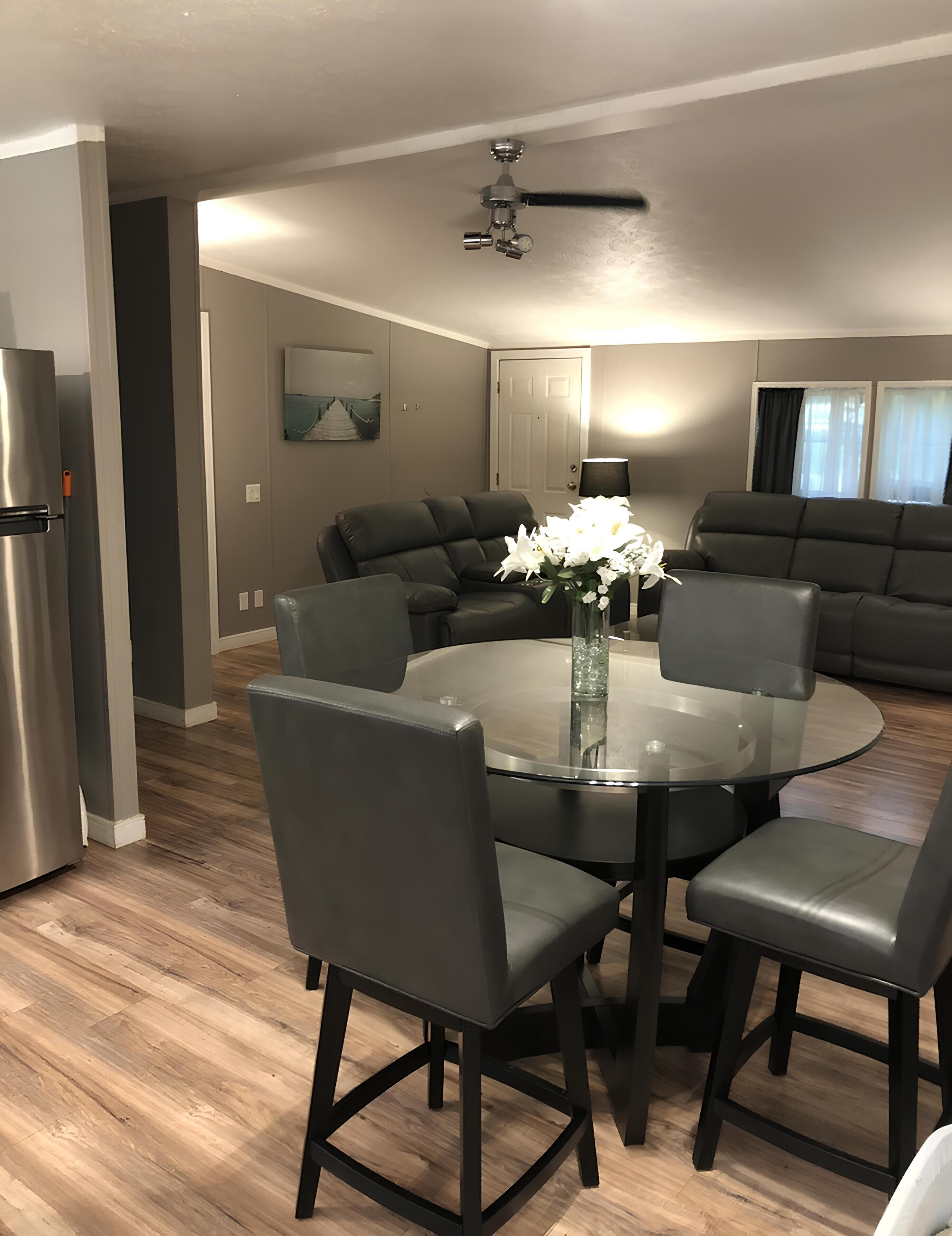 A modern kitchen with a dining table, chairs, a refrigerator, and a ceiling fan.
