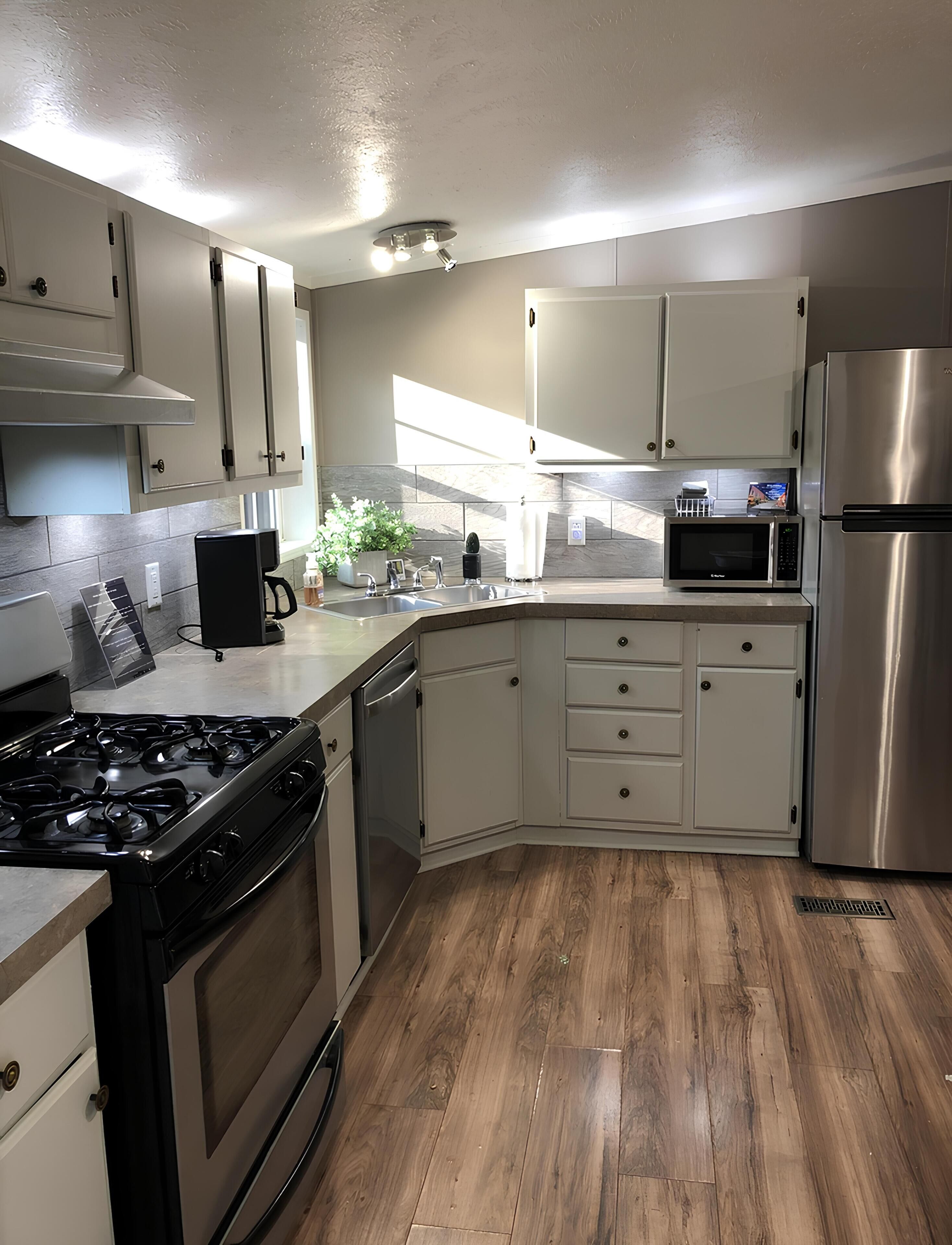 A kitchen with white cabinets, a stainless steel refrigerator, a microwave, a stove, and a dishwasher.