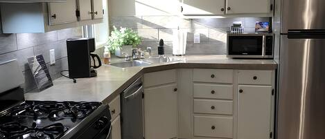 A kitchen with white cabinets, a stainless steel refrigerator, a microwave, a stove, and a dishwasher.