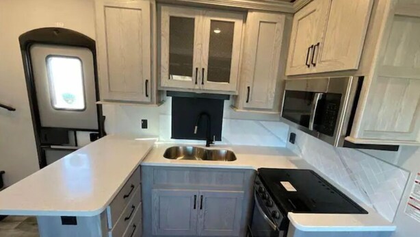 Una cucina compatta con mobili bianchi, un lavello nero, un fornello e un microonde.