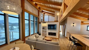 A modern living room with a large sofa, a dining table, and a kitchen area with a bar. - Meridian Lake- Mountain Modern (Crested Butte)