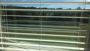 A view through a window with horizontal blinds, revealing a building and a landscape with trees and a clear sky. - quiet, cozy, country loft close to everything (Sherwood)