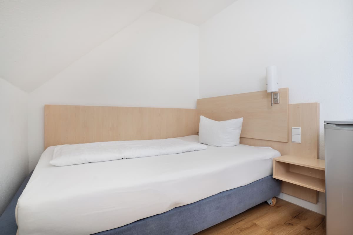 A single bed with a wooden headboard, a bedside table, and a wall-mounted light fixture.