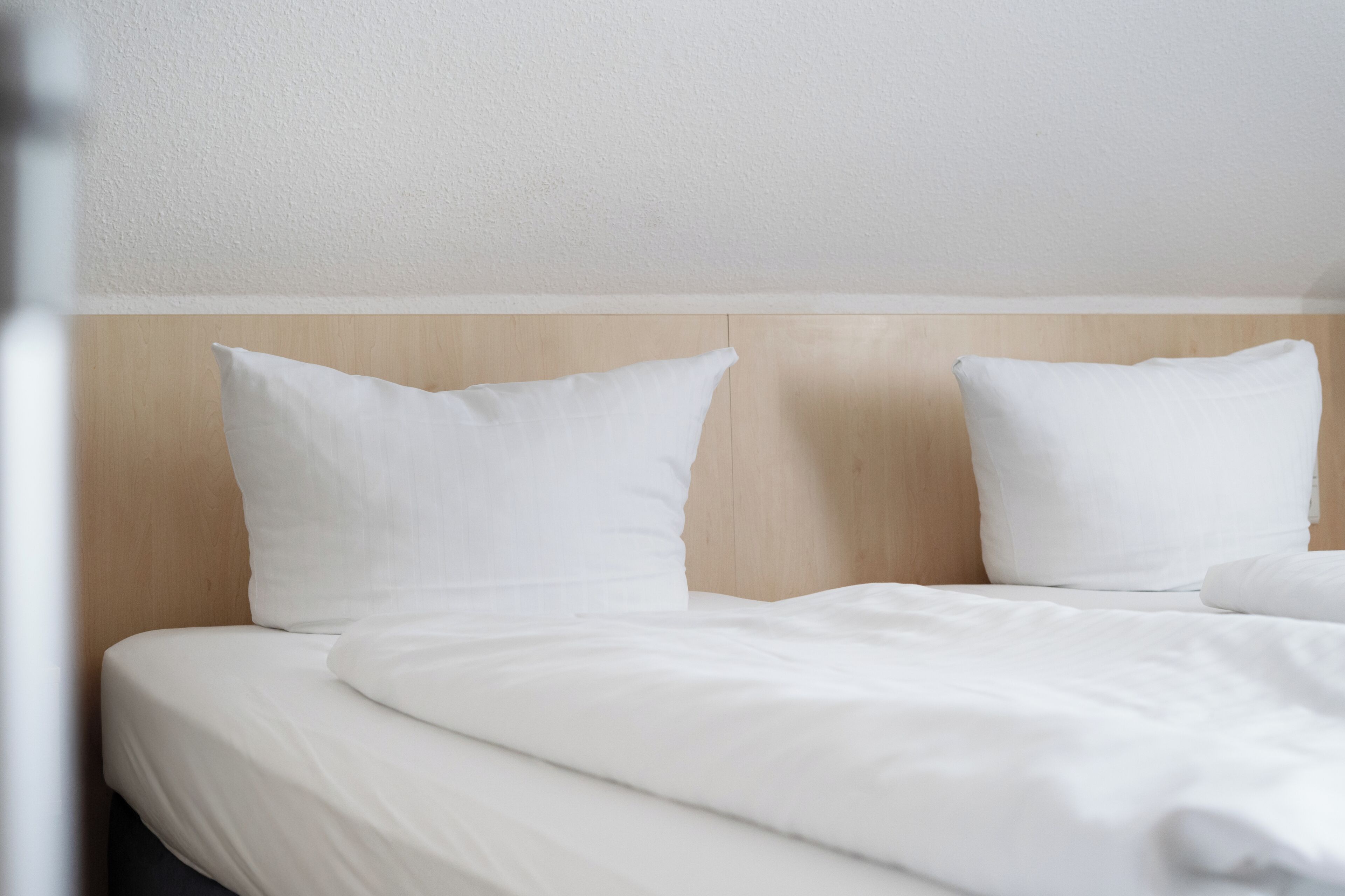 Une chambre d’hôtel avec une tête de lit en bois, du linge de lit blanc et un design épuré et minimaliste.