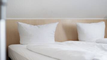 Une chambre d’hôtel avec une tête de lit en bois, du linge de lit blanc et un design épuré et minimaliste.