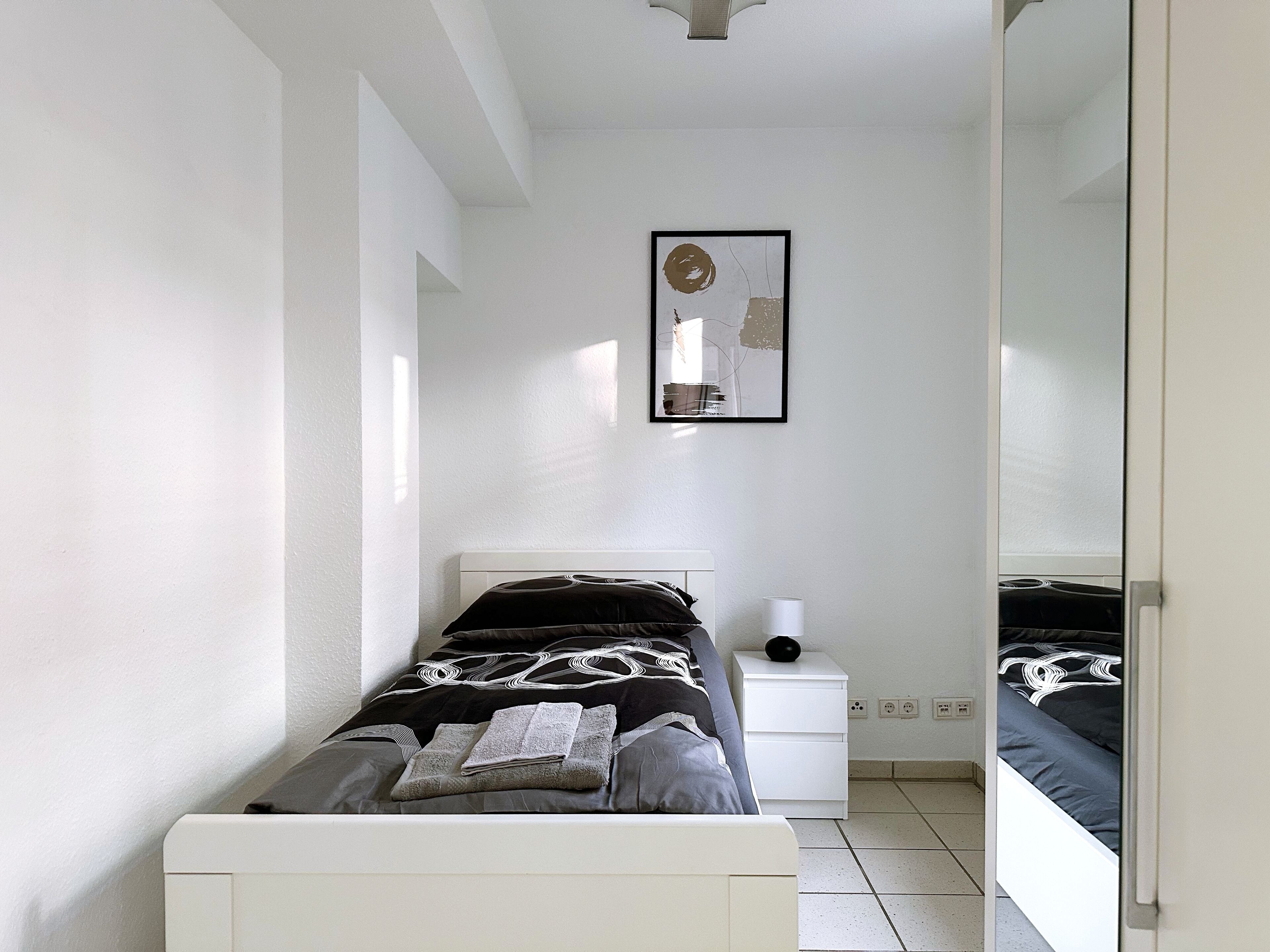 Ein Schlafzimmer mit einem Bett, einem Nachttisch, einem Wandbild und einem Spiegel.