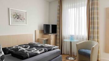 Habitación de hotel con cama, televisión, mesita, una silla y ventana con cortinas.